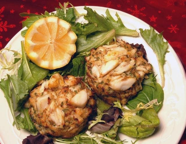 2 crab cakes on a bed of lettuce served with a lemon